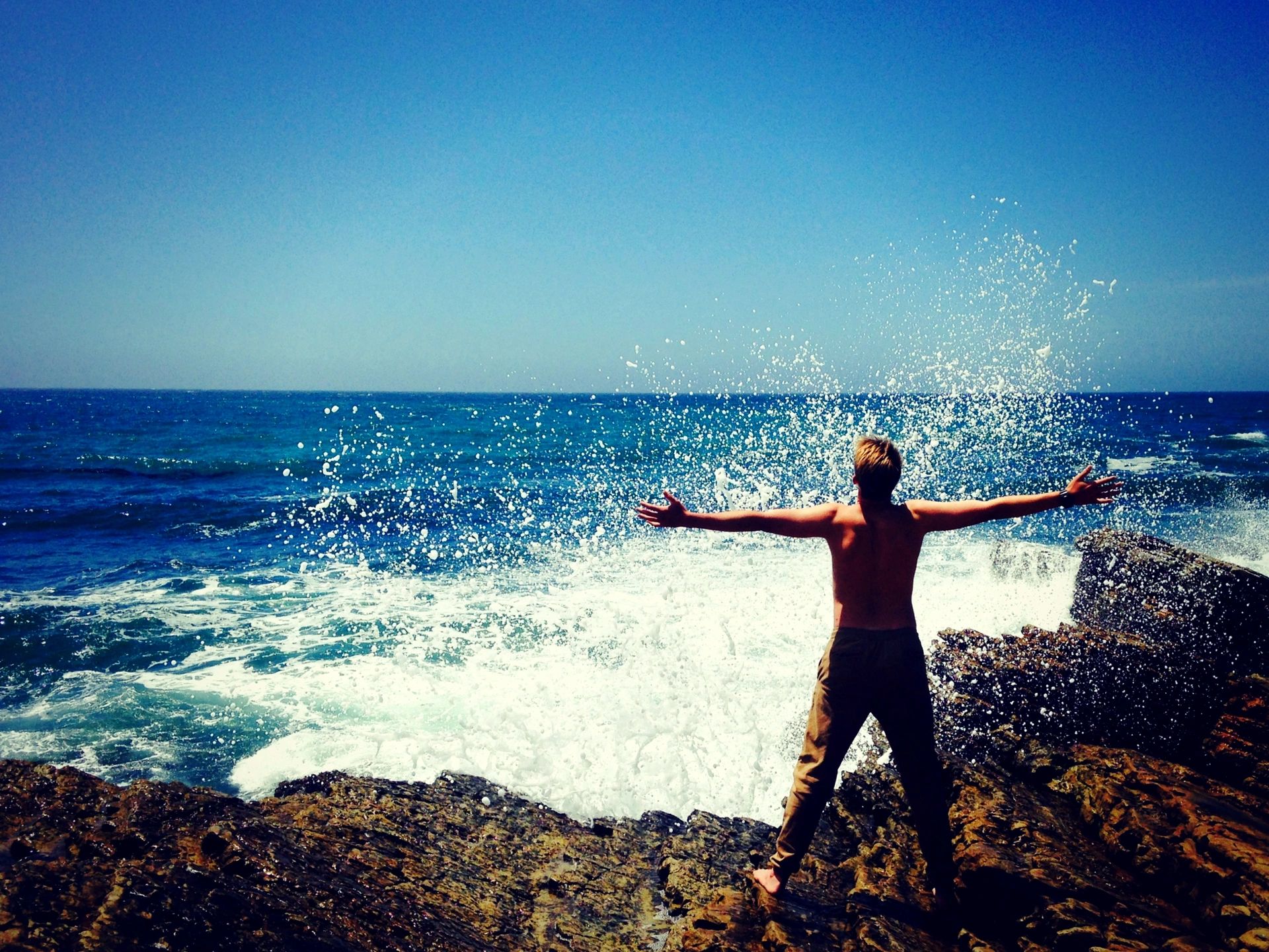 A happy man stands on the beach with his arms wide open, facing the sea, enjoying the breeze and the serenity of the ocean.